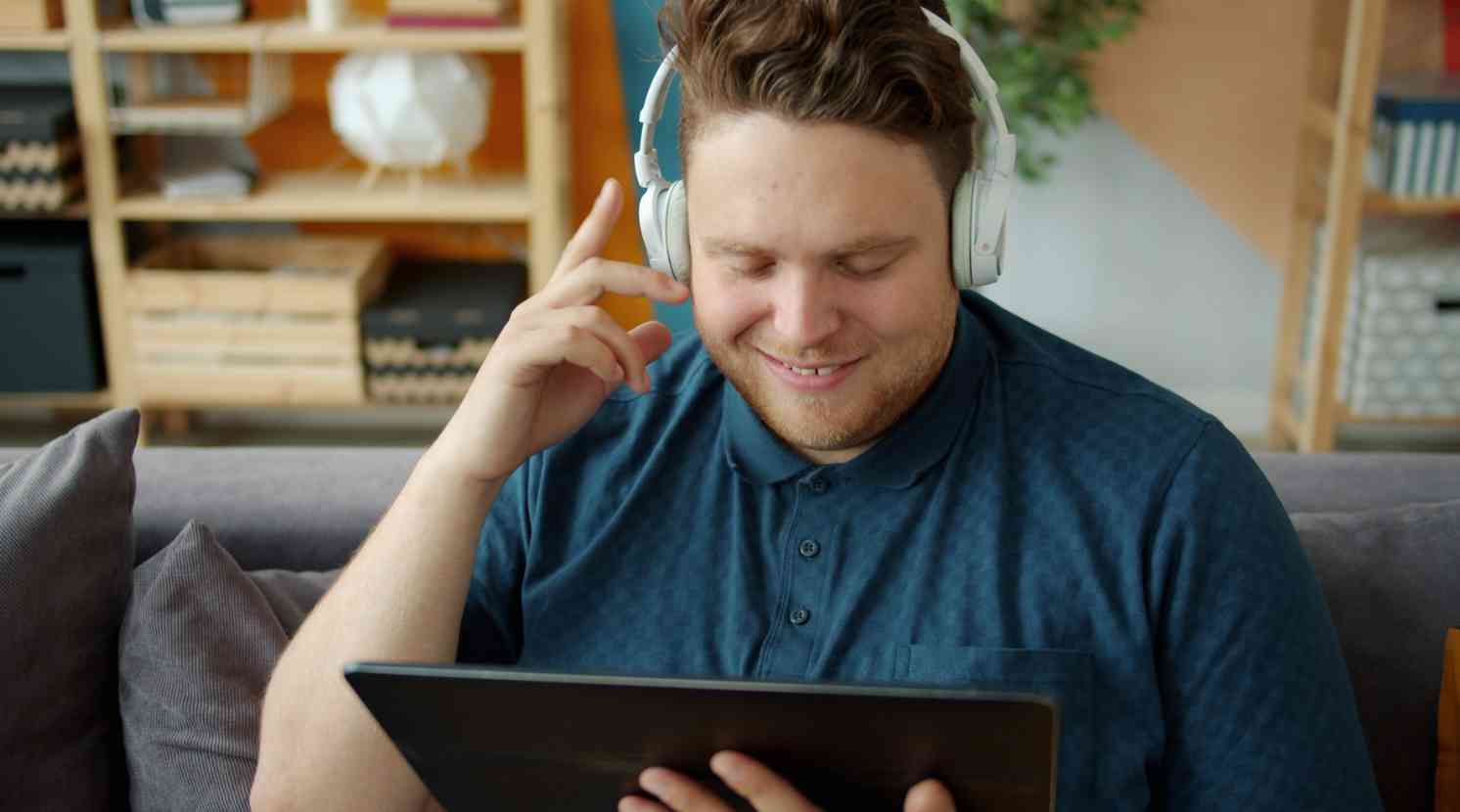 Mann sitzt auf der Couch am Laptop und hat Kopfhörer auf